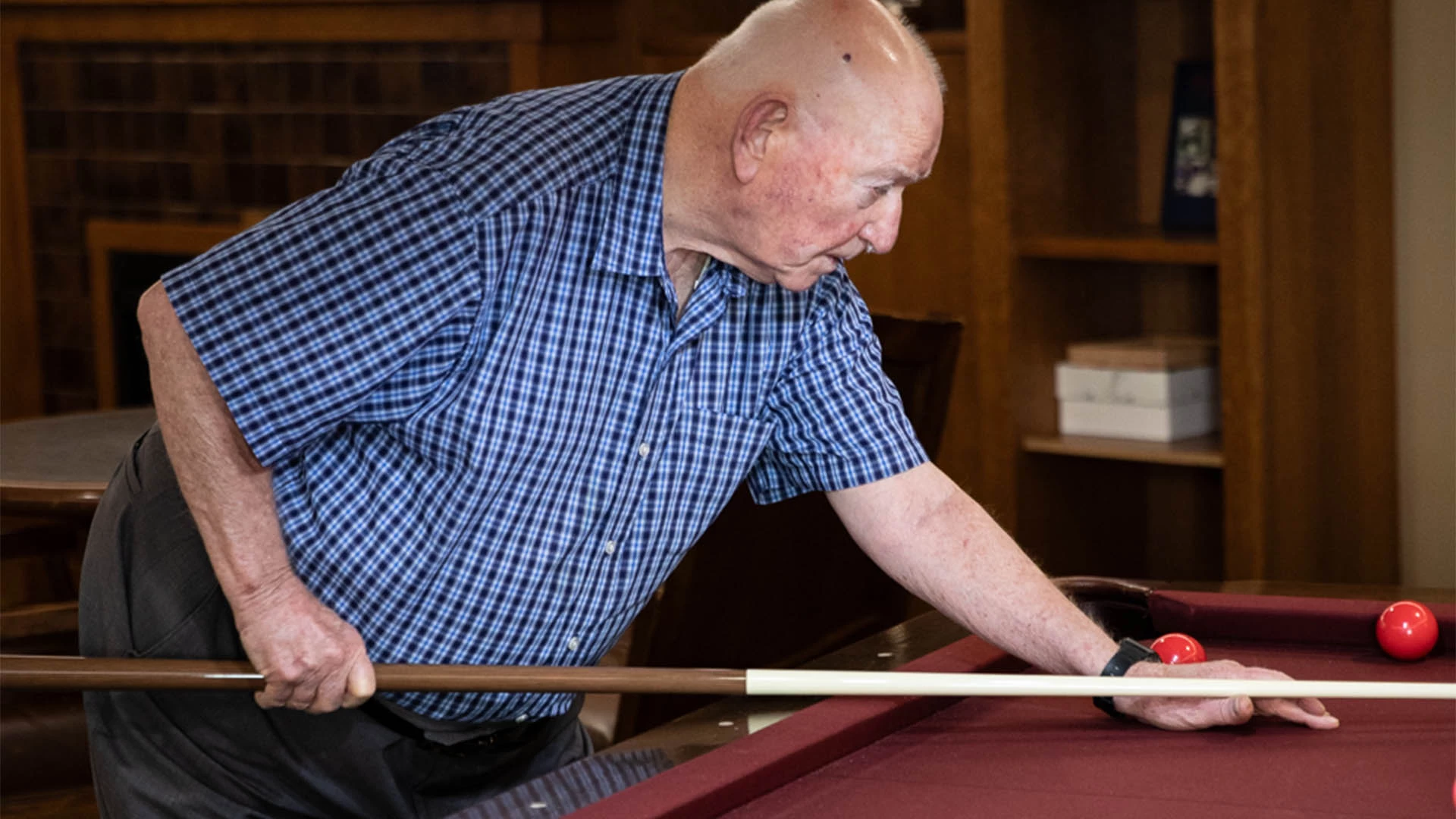 Senior male in blue plaid shirt playing billiards