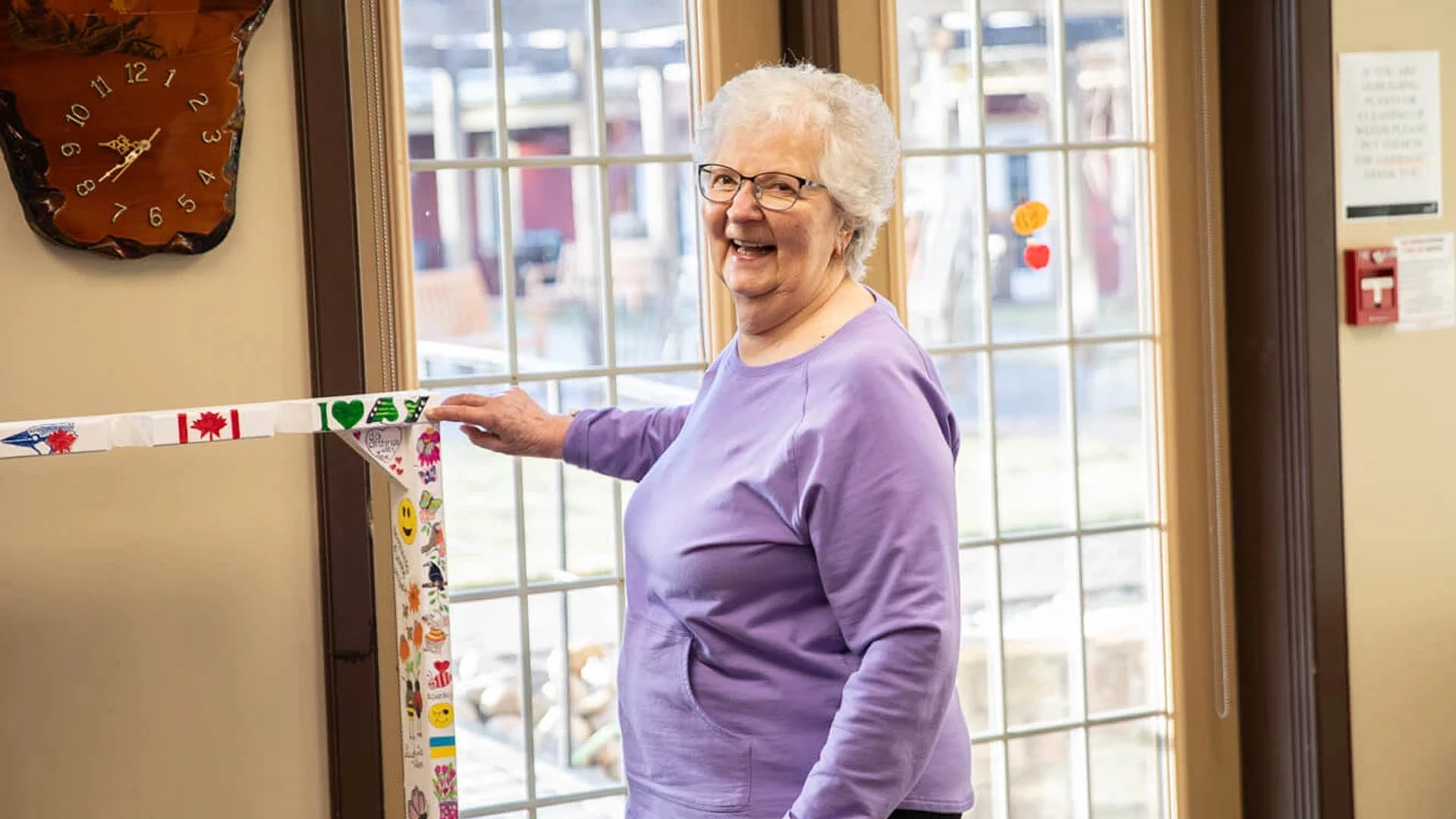 Elderly woman in a purple shirt pointing at a sticker and smiling